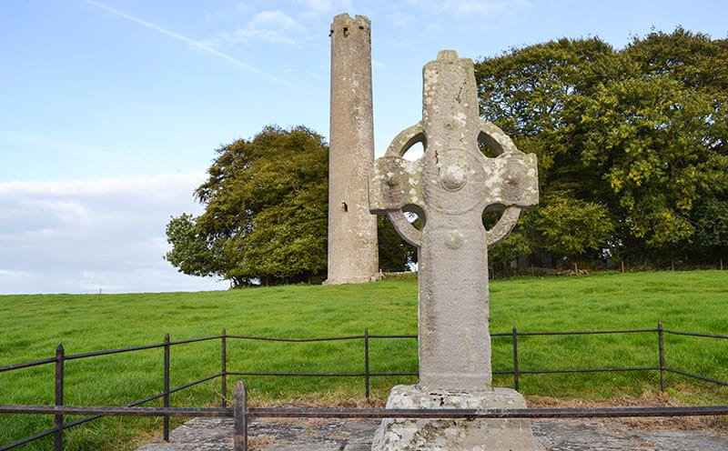 The High Cross at Kilree with the Round Tower and Monastic Site across the field in the background - The Irish Place